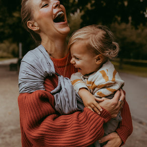 Ein tiefes Lachen aus dem Bauch heraus mit ihrem Kleinkind in ihrem zeitlosen grauen Mondring-Tragetuch